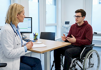 Junger Mann im Rollstuhl ist zu einem Annamnesegespräch bei seiner behandelnden Ärztin.