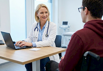 Eine Ärztin spricht mit einem jungen Patienten im Rollstuhl über die Ergebnisse seiner Untersuchung..