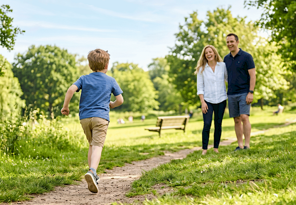 Ein kleiner Junge rennt im Park zu seinen Eltern – Symbolbild einer Familie, dessen Kind an Hämophilie erkrankt ist und trotzdem ein weitgehend normales Leben führt.